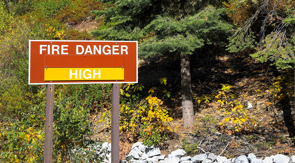 large red sign that says FIRE DANGER HIGH with a wooded background